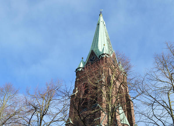 Der hohe Kirchturm mit dem grünen Dach ragt in den blauen Himmel.