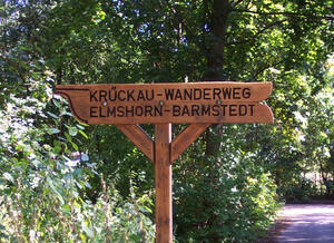 Der Wegweiser aus Holz trägt die Beschriftung Krückau-Wanderweg, Elmshorn-Barmstedt.