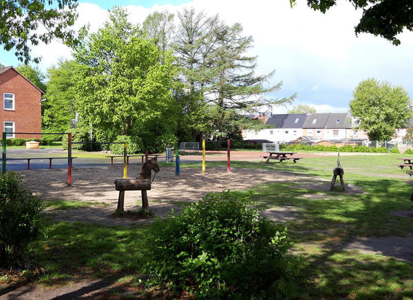 Holzpferde, Reckstangen, ein Sandplatz und ein paar grüne Bäume sind hier abgebildet.
