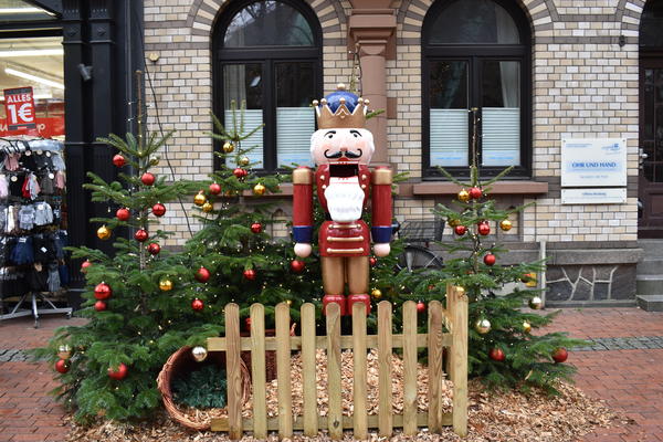 Lebensgroßer traditioneller Holz-Nussknacker umgeben von weihnachtlich geschmückten Tannen.
