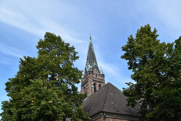 Der Kirchturm der St. Nikolai-Kirche ragt zwischen Bäumen in den Himmel.