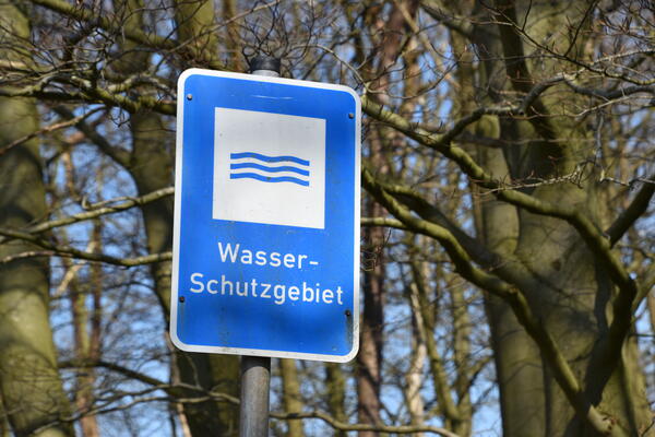 Schild mit der Aufschrift Wasser-Schutzgebiet. Im Hintergrund sind kahle Baumstämme.