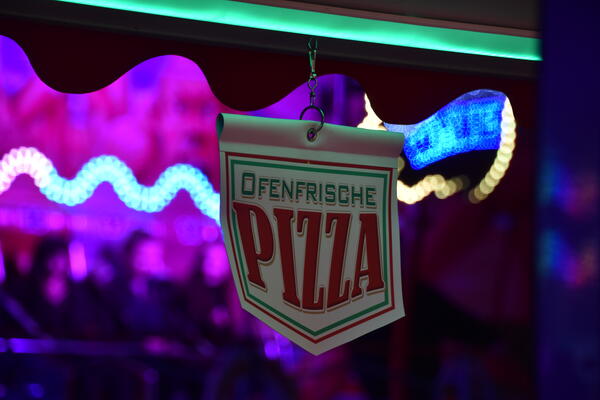 Ein kleines Schild vor bunten Lichtern bietet ofenfrische Pizza an.