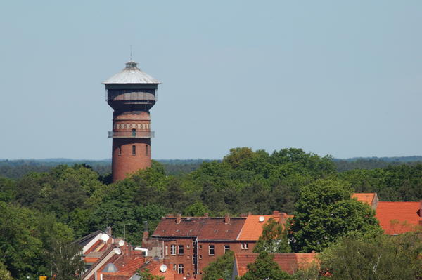 Blick über die Dächer von Wittenberge auf den, von Bäumen und Büschen umzingelten, Wasserturm.