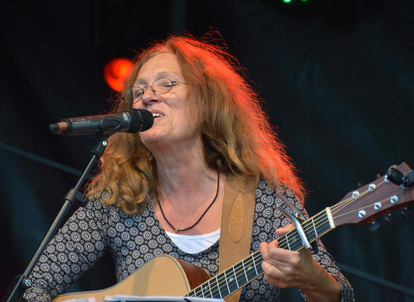 Bild vergr&ouml;&szlig;ern: Die S&auml;ngerin singt ausdrucksvoll in ein Mikrofon und spielt dazu Gitarre.