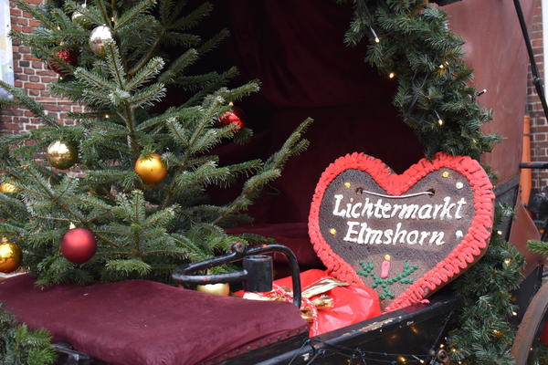 Lebkuchenherz mit dem Schriftzug "Lichtermarkt Elmshorn" auf einer weihnachtlich geschmückten Kutsche.