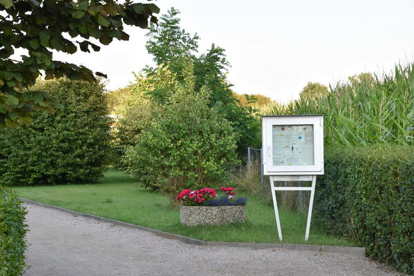 Eine Hinweistafel steht vor einer großen Hecke in der Kleingartenanlage Am Pfahlkrug .