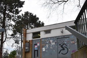 Bild vergr&ouml;&szlig;ern: Teilansicht einer WC-Anlage mit Metallfront und Metallt&uuml;ren. Auf einer T&uuml;r ist ein gro&szlig;es Symbol f&uuml;r Rollstuhlfagrende. Die WC-Anlage ist mit Aufklebern &uuml;bers&auml;t.