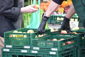 Bild vergr&ouml;&szlig;ern: Kisten mit &Auml;pfeln an einem Verkaufsstand auf dem Buttermarkt. Der Verk&auml;ufer tr&auml;gt Schutzhandschuhe.