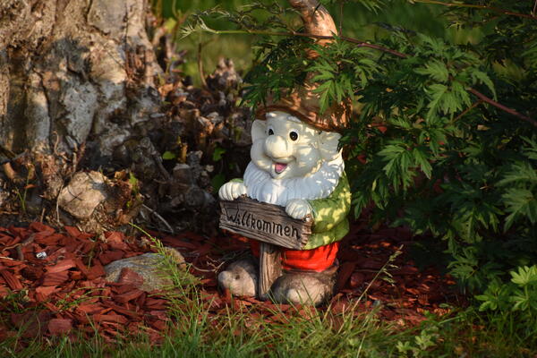 Ein Gartenzwerg mit roter Zipfelmütze hält ein Holzschild mit dem Schriftzug Herzlich Willkommen.