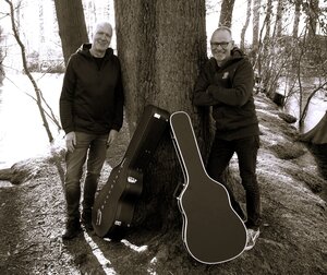 Bild vergr&ouml;&szlig;ern: Abbildung von zwei l&auml;chelnden M&auml;nnern hinter Gitarrenkoffern neben einem Baum in einer Darstellung in schwarz-wei&szlig;.