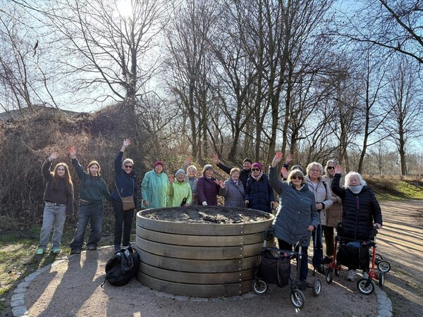 Bild vergr&ouml;&szlig;ern: Frauen und M&auml;nner werben f&uuml;r Bewegungsangebote f&uuml;r Seniorinnen und Senioren. Im Hintergrund sind laublose B&auml;ume zu sehen.