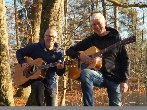 Zwei M&auml;nner stehen mit Gitarre im Wald.