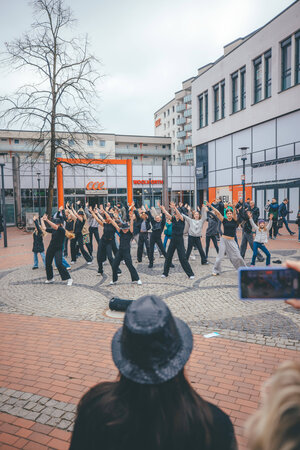Bild vergr&ouml;&szlig;ern: Eine Gruppe aus sechs schwarz gekleideten T&auml;nzerinnen performt auf dem Alten Markt in Elmshorn, rundherum stehen Menschen und gucken zu.