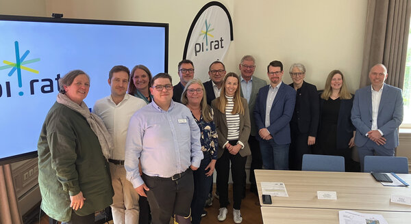 Bild vergr&ouml;&szlig;ern: Gruppenfoto vor einem Bildschirm mit PI.Rat darauf.