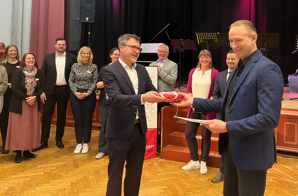 Bild vergr&ouml;&szlig;ern: Frauen und M&auml;nner vor einer B&uuml;hne. Oberb&uuml;rgermeister Erik Sachse &uuml;berreicht dem scheidenden Ersten Stadtrat Dirk Moritz ein Geschenk.