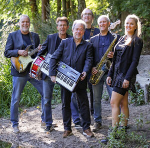 Die sechs Musiker*innen stehen zusammen mit ihren Instrumenten im Wald und posieren lächelnd für die Kamera.