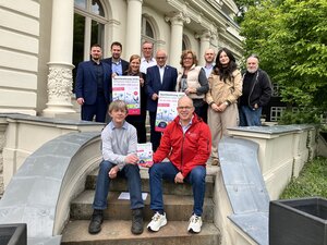Bild vergr&ouml;&szlig;ern: Frauen und M&auml;nner vor der Wei&szlig;en Villa in Elmshorn, die f&uuml;r die Sportlehrung am 29. Mai 2026 werben.