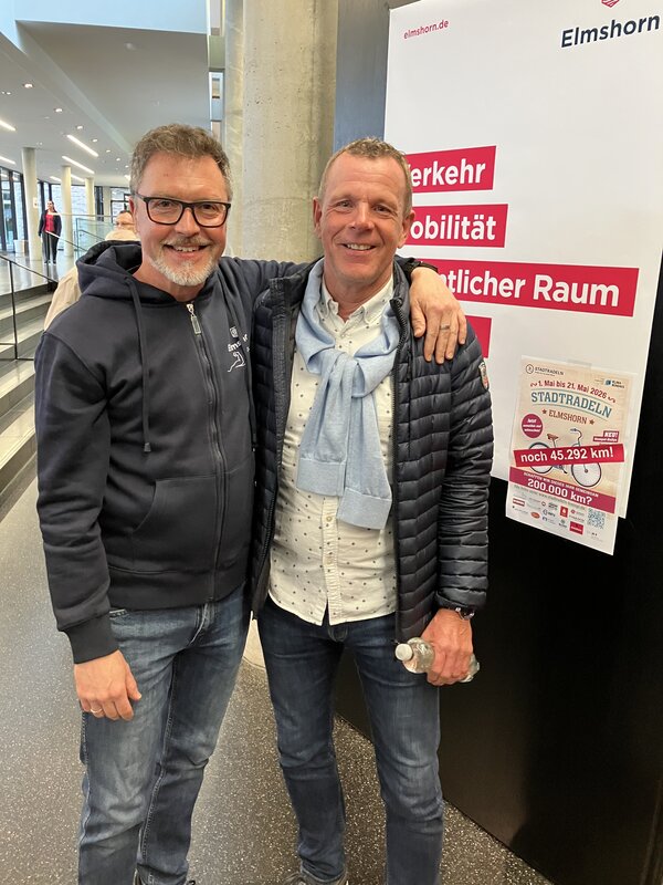 Bild vergr&ouml;&szlig;ern: Zwei M&auml;nner stehen Arm in Arm im Foyer.