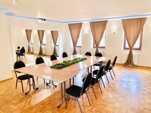 Bild vergr&ouml;&szlig;ern: Innenansicht eines Seminarraums mit einer Tischtafel und zehn St&uuml;hlen vor gebundenen Vorh&auml;ngen.
