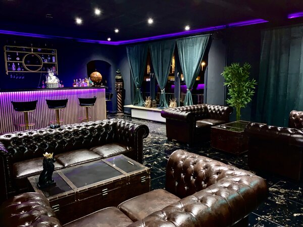Bild vergr&ouml;&szlig;ern: Innenansicht eines Loungebereiches mit schweren Ledersofas vor einer Bar mit Barhockern.