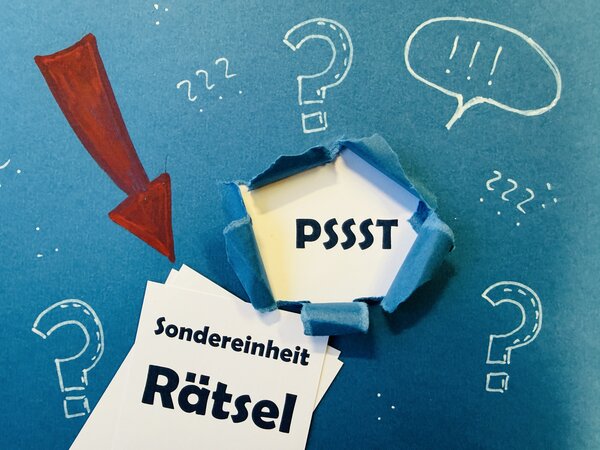 Mit Symbolen beschriebene blaue Tafel, worauf die Worte "Pssst" und "Sondereinheit R&auml;tsel" auf wei&szlig;em Grund hervorgehoben sind.