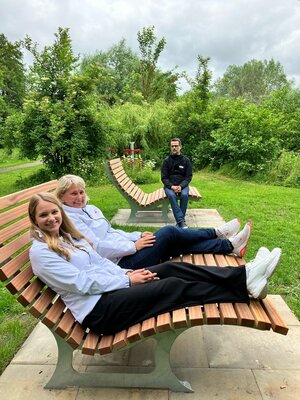 Bild vergr&ouml;&szlig;ern: Drei Personen pr&auml;sentieren neue fest installierte Sonnenliegen in einem Park.