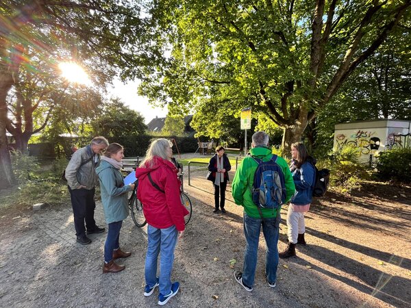 Frauen und M&auml;nner in einer park&auml;hnlichen Anlage mit B&auml;umen und Kieswegen