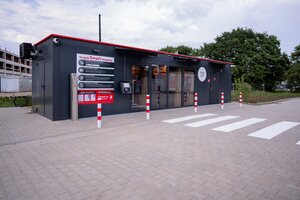Bild vergr&ouml;&szlig;ern: Ein Smart Shop untergebracht in einem Container &auml;hnlichen Geb&auml;ude -  davor Markierungspfosten und ein Zebrastreifen f&uuml;r die sichere Zuf&uuml;hrung zum Eingang.
