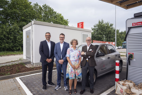 Bild vergr&ouml;&szlig;ern: Der neue ORLEN Charge E-Ladehub in Elmshorn nahe der A23 in der Werner-von-Siemens-Stra&szlig;e mit vier Personen, die vor einem Fahrzeug an einem Ladepunkt stehen.
