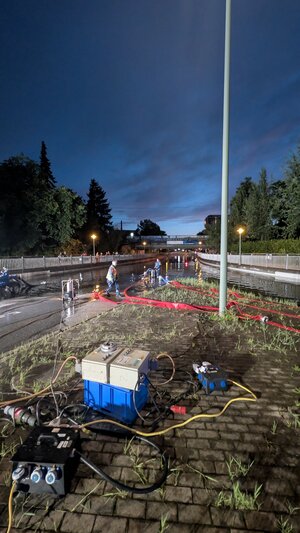 Bild vergr&ouml;&szlig;ern: Schl&auml;uche liegen am Boden vor der vollgelaufenen Bahnunterf&uuml;hrung Hamburger Stra&szlig;e.