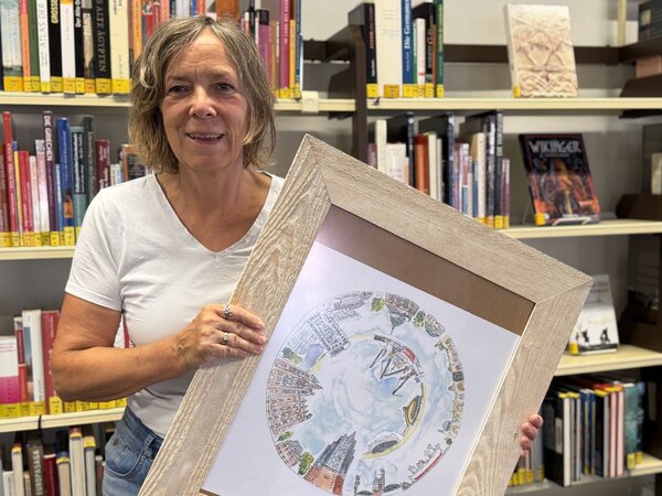 K&uuml;nstlerin Ilka Sch&uuml;mann mit einem ihrer Bilder in der Hand vor einem B&uuml;cherregal in der Stadtb&uuml;cherei, in der sie einige ihrer Arbeiten ausstellt.