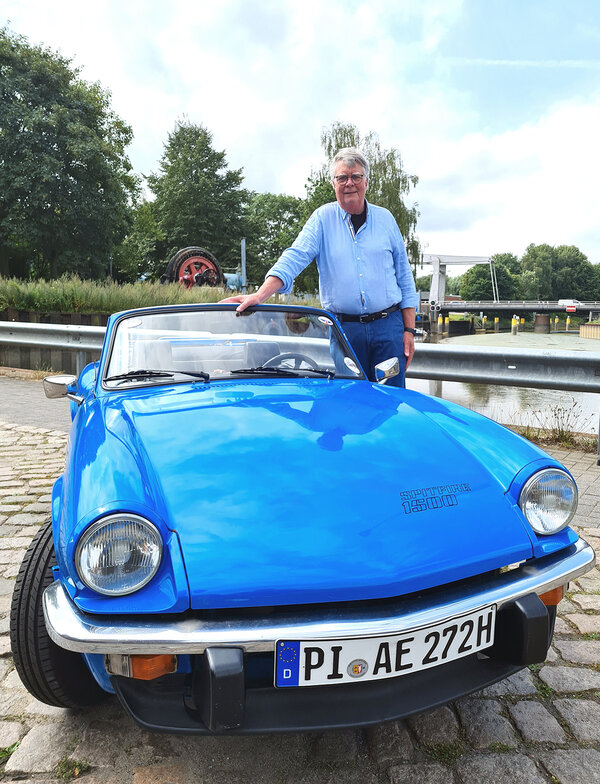 Ein Mann im Hemd lehnt an seinem blauen Cabrio.