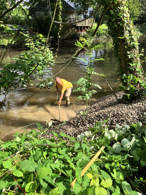 Bild vergr&ouml;&szlig;ern: Person verteilt Kies am Kr&uuml;ckau-Ufer und in der Kr&uuml;ckau.