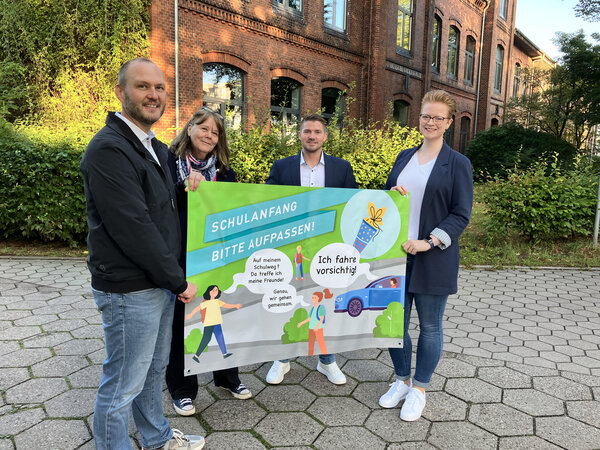 Bild vergr&ouml;&szlig;ern: Erster Stadtrat Michael Leeske h&auml;lt mit drei weiteren Personen vor der Hafenschule Elmshorn ein Plakat hoch, das f&uuml;r mehr Sicherheit auf den Schulwegen pl&auml;diert.