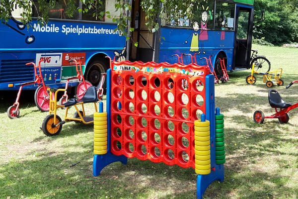 Bunte Spiele im Großformat sowie besondere Dreiräder vor dem auffälligen Bus der mobilen Spielplatzbetreuung.