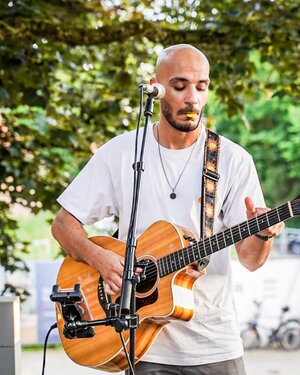 Bild vergr&ouml;&szlig;ern: Ein Mann mit Glatze spielt Gitarre an einem Mikro auf einem St&auml;nder.