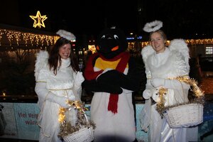 Bild vergr&ouml;&szlig;ern: Zwei Weihnachtsengel und ein verkleideter Pinguin vor der Eisfl&auml;che des Stadtwerke Eisvergn&uuml;gens auf dem Holstenplatz.
