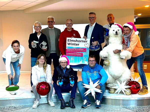 Bild vergr&ouml;&szlig;ern: 10 Personen mit Winterdekogegenst&auml;nden und ein gro&szlig;er k&uuml;nstlicher Eisb&auml;r posieren mit Plakat f&uuml;r das Stadtwerke Eisvergn&uuml;gen.