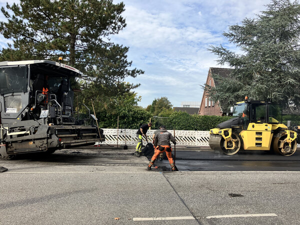 Bild vergr&ouml;&szlig;ern: Bauarbeiter verteilen hei&szlig;en Asphalt auf einer Stra&szlig;e.