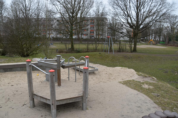 Neben einer Wiese stehen auf einem Sandplatz eine Spiel-Wasser-Rinne in verschiedenen Höhen. Im Hintergrund ist eine Seilbahn.