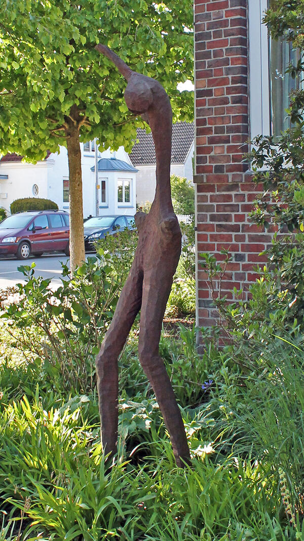 Das Kunstwerk des Künstlers Erik Barran befindet sich am Hogenkamp 16. Die Figur in rostbraunem Ton, in leicht gebeugter Haltung, steht in einem Vorgarten