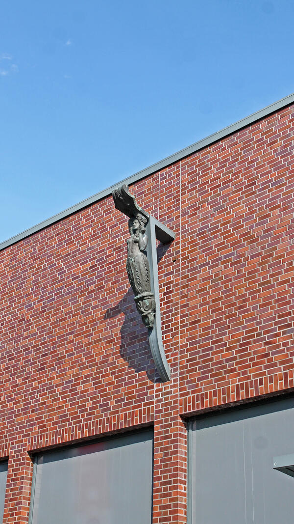 Das Kunstwerk von Wilhelm Petersen befindet sich an der Volksbank Berliner Straße mit der Bezeichnung Flora. Es ist aus dem Jahr 1969. Die Galionsfigur eines Schiffes hängt an einer Gebäudefassade aus roten Steinen.