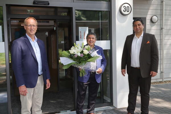 Bügermeister Hatje mit den beiden Geschäftsführern vor dem Eingang ihrs Hotels mit einem großen Blumenstrauß in der Hand.