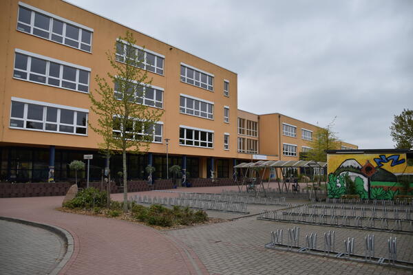 Viele Fahrradständer stehen vor dem Ockerfarbenen Schulgebäude.