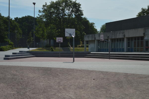 Auf einem Sportplatz stehen drei Basketballkörbe gegenüber.