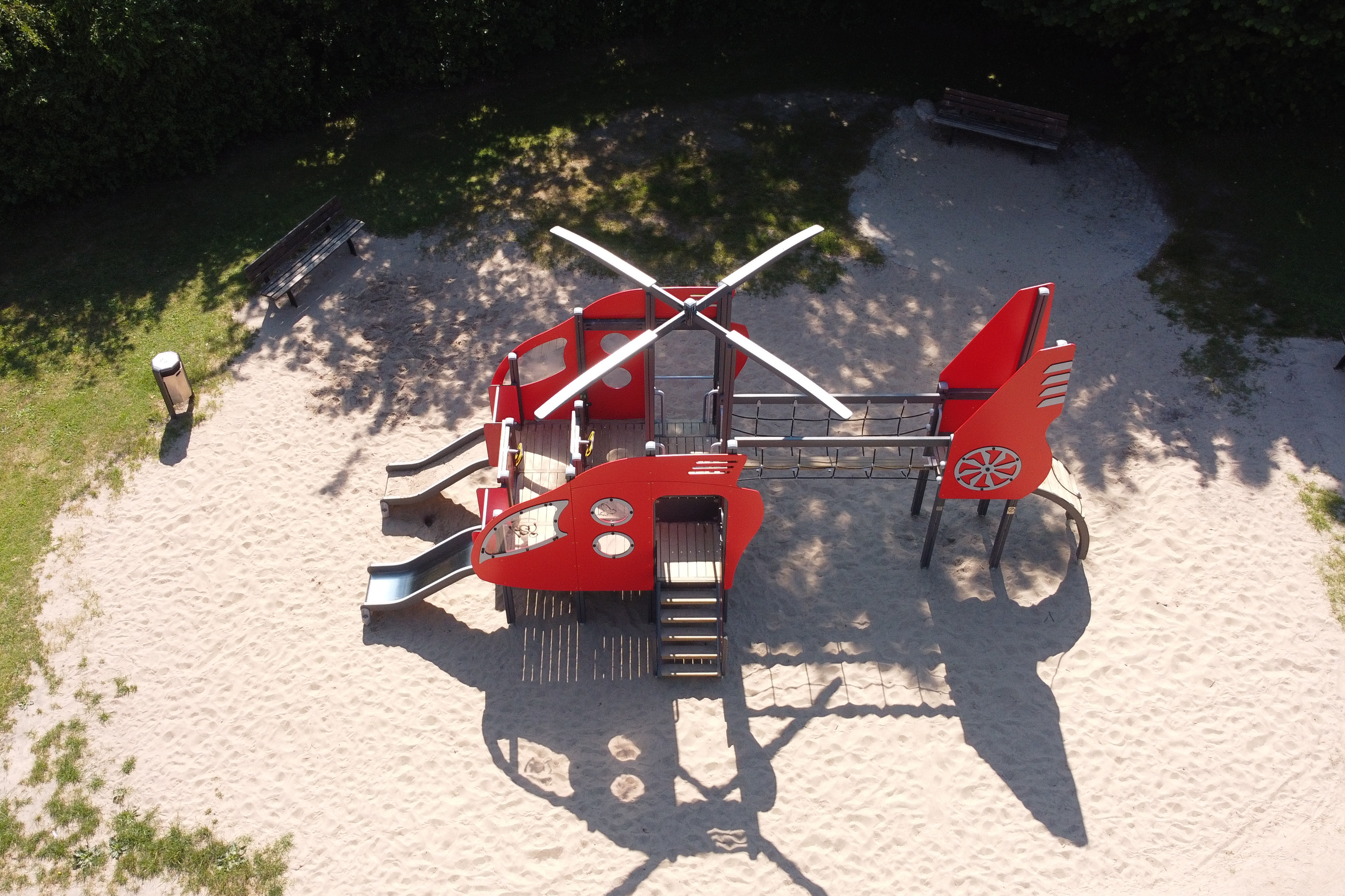 Auf einem Sandplatz steht ein Klettergerüst in Form eines roten Hubschraubers.