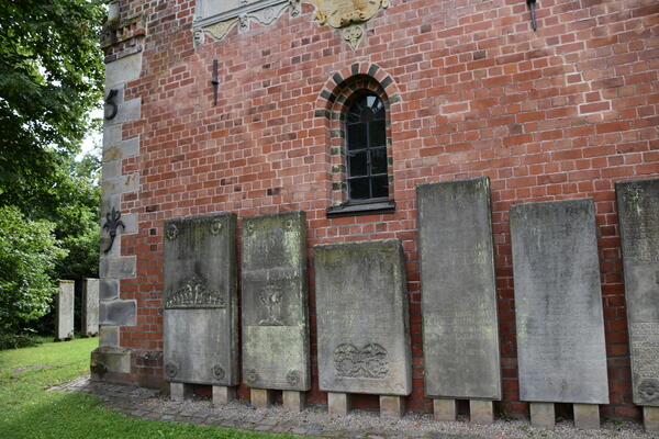Große, historische Steintafeln lehnen an dem roten Backsteingebäude.