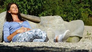Eine Frau sitzt an einen Stein gelehnt und sonnt sich.