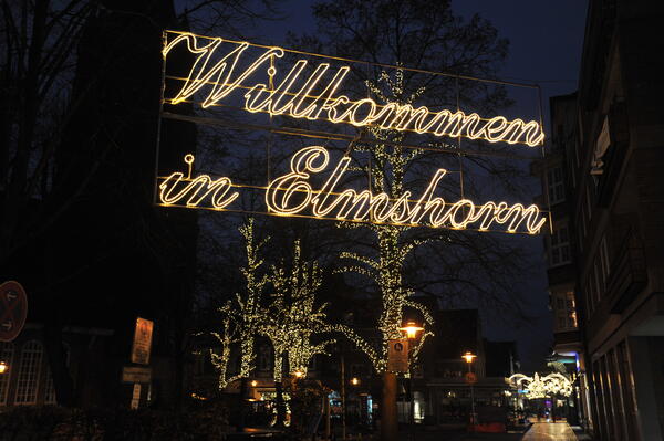 Erleuchteter Schriftzug "Willkommen in Elmshorn" mit beleuchteten Bäumen rund um den Alten Markt und die Nikolaikirche.